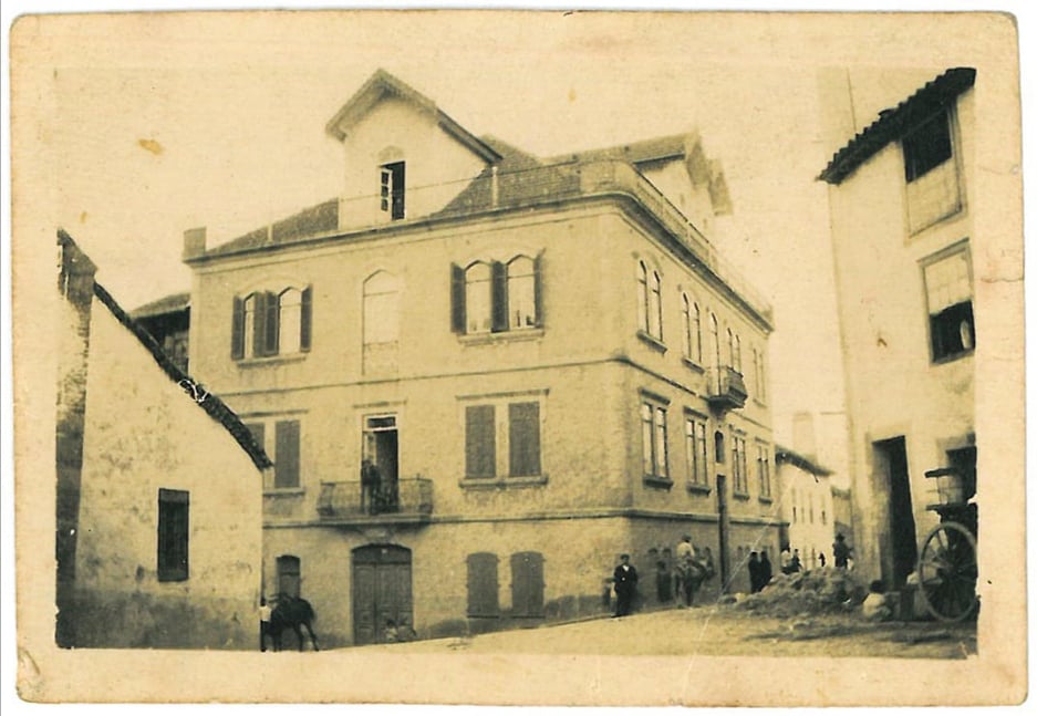 Fotografia a preto e branco, amarelada, da casa de João Alves da Silva, personalidade marcante da história da Covilhã, que foi o antigo liceu municipal, com o edifício oposto, à direita, em obras e algumas pessoas na rua.