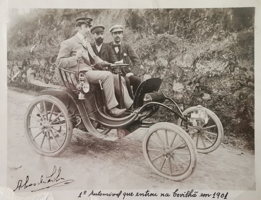 Fotografia a preto e branco, em tons de sépia, da primeira subida à Serra da Estrela em automóvel, protagonizada em 1906 por João Alves da Silva, personalidade marcante da história da Covilhã, assinada pelo próprio, fotografado ao volante, e com a inscrição "1º Automóvel que entrou na Covilhã em 1901". Estão presentes mais dois indivíduos, apeados, não identificados.